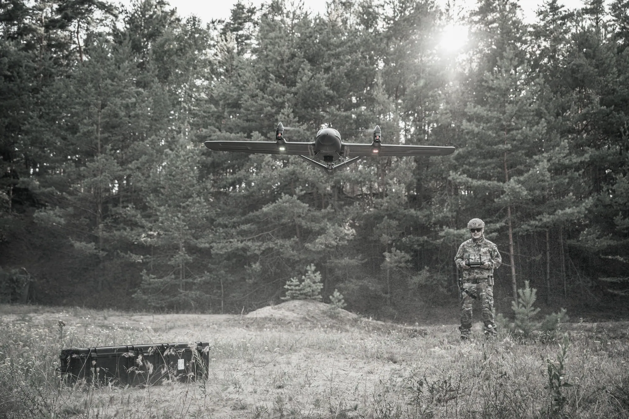 Fixed-wing UAS in flight over a clearing with its operator